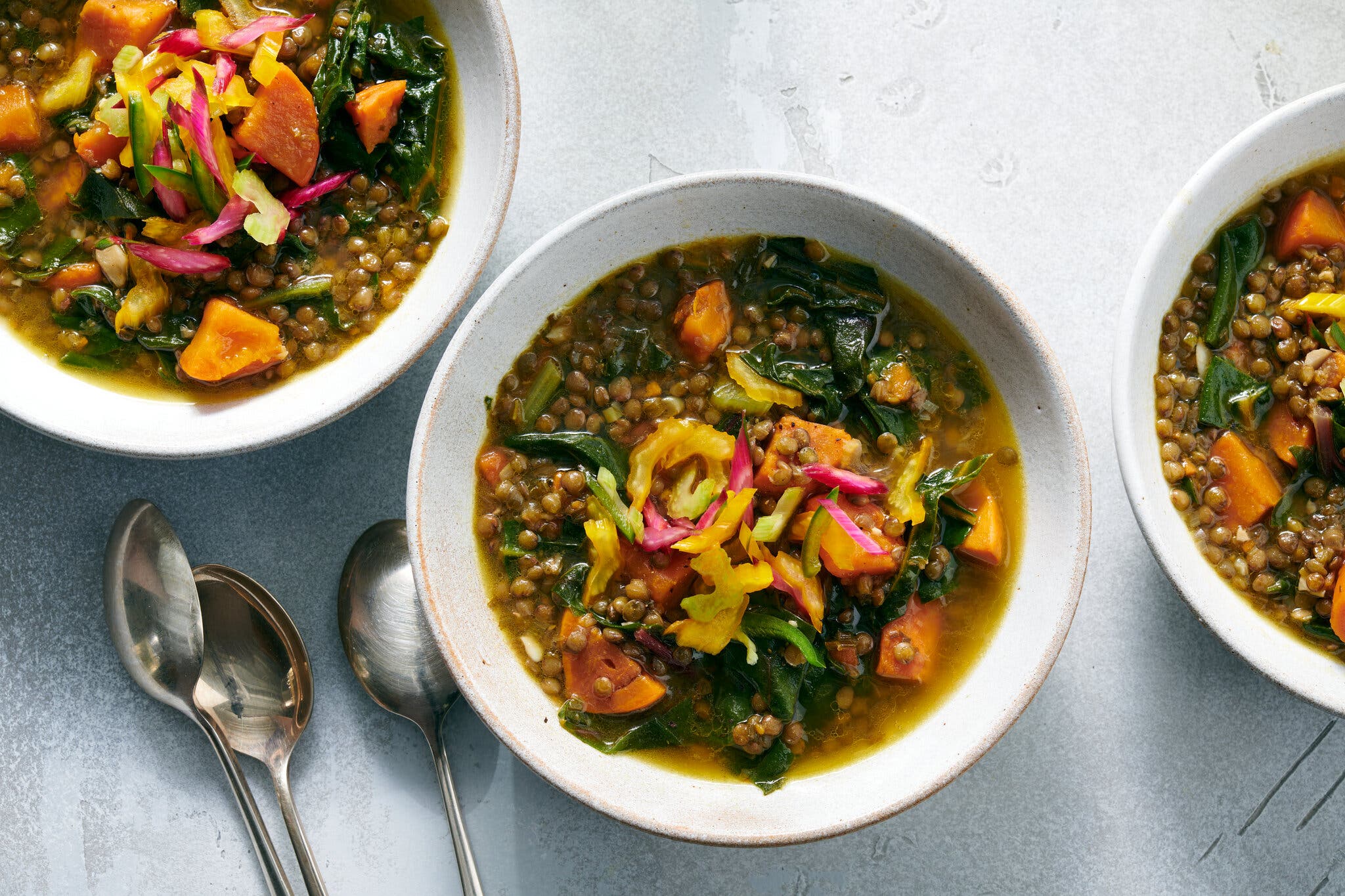 An overhead image of three bowls of lentil soup topped with vegetables.