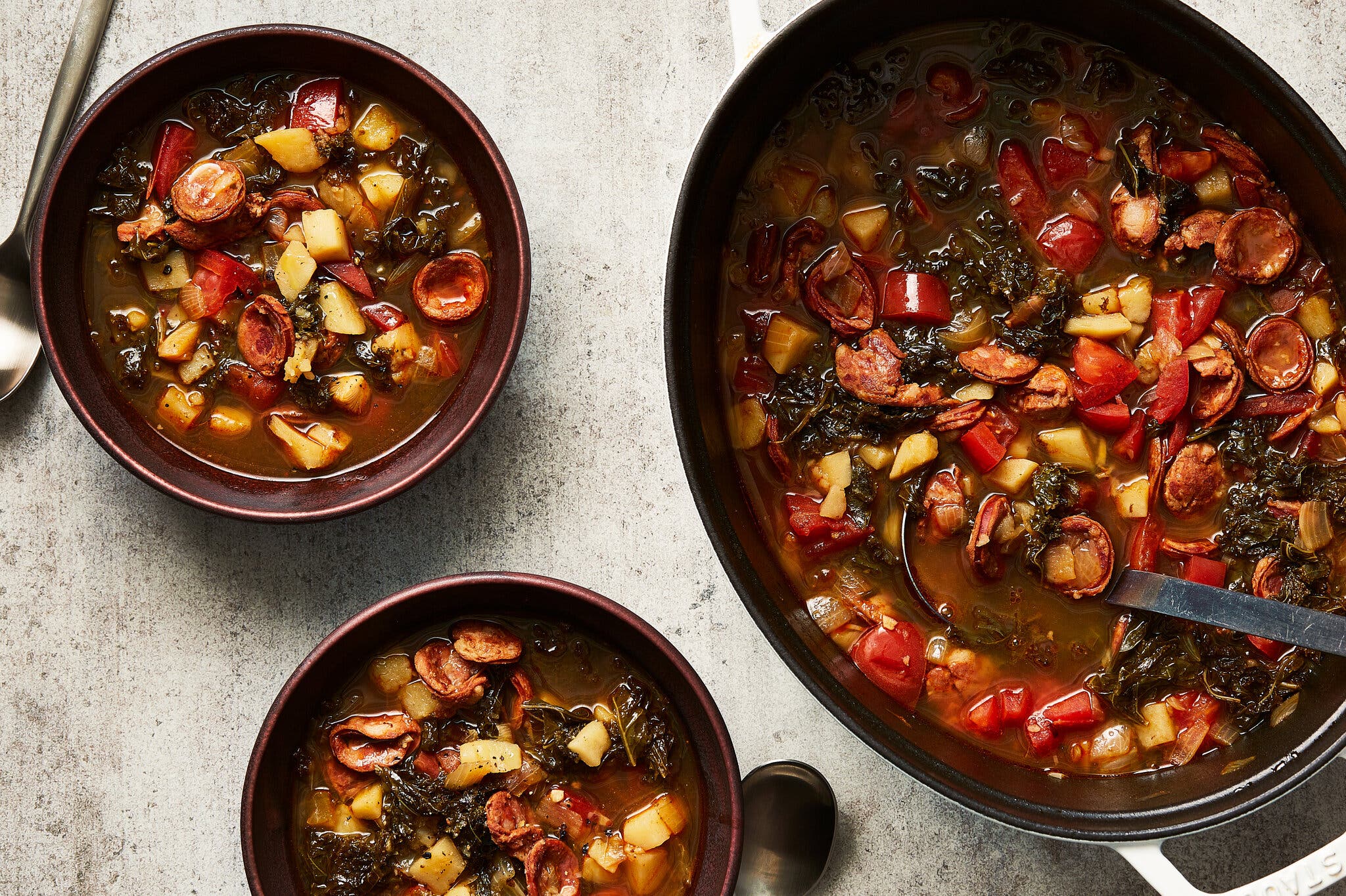 A kale soup sits in a large pot next to two bowls filled with the soup. A ladle sticks out of the pot.