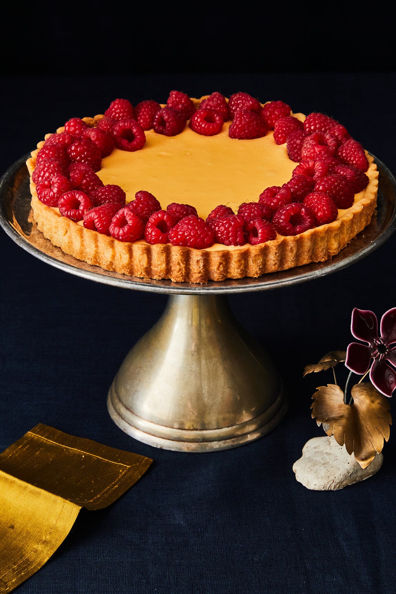 A yellow tart ringed with raspberries is photographed at 3/4 of an angle.