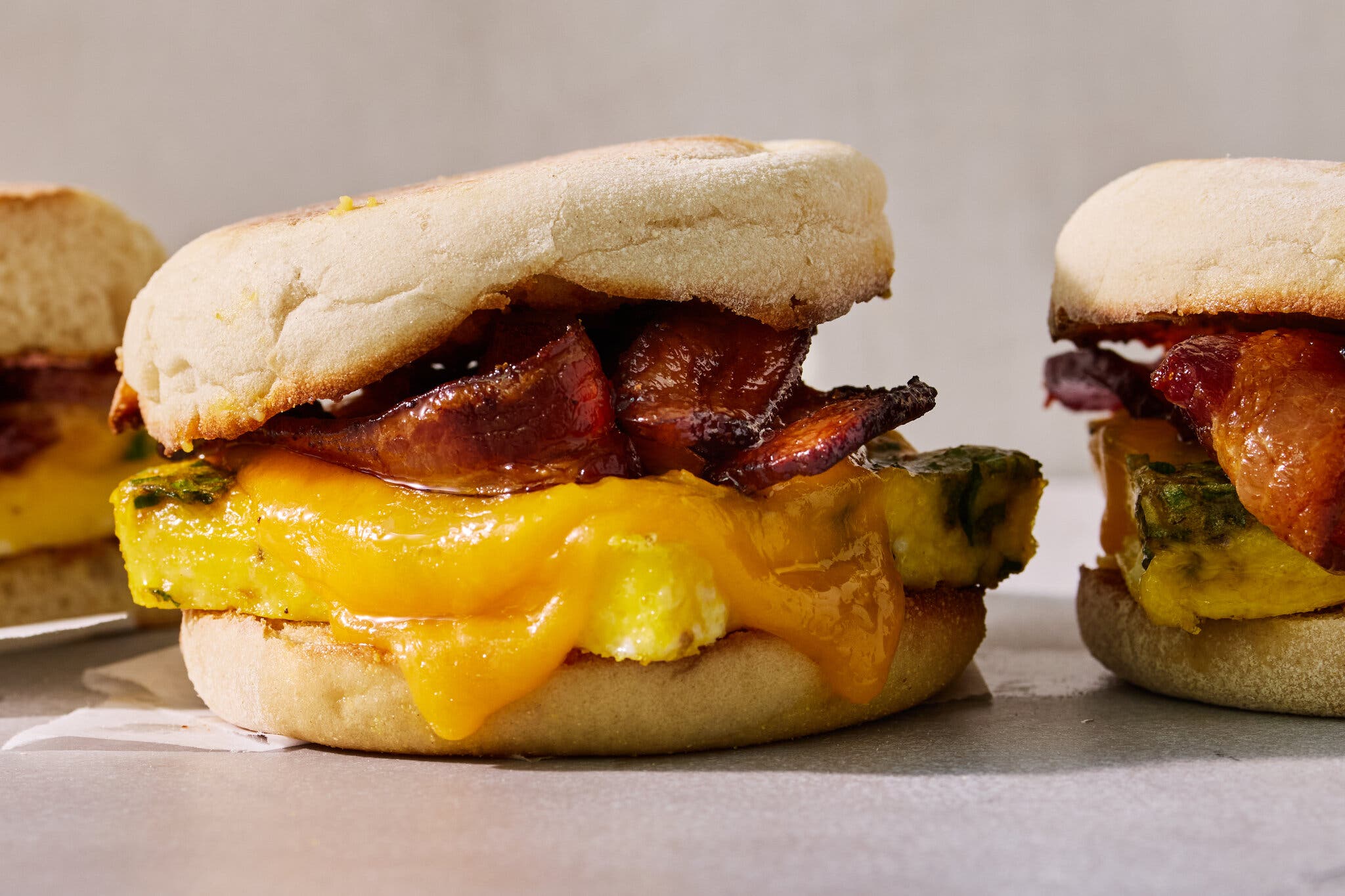 Two English muffin breakfast sandwiches containing egg patties, melted orange cheese and crispy bacon.