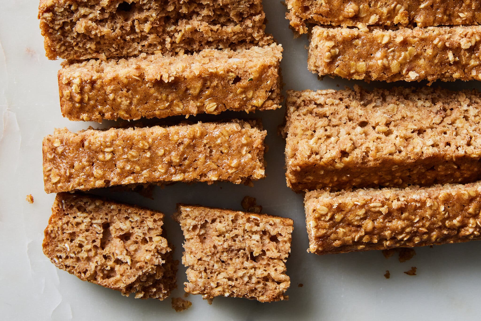 Golden brown oat bars, one of which is broken, arranged on a light-colored surface.