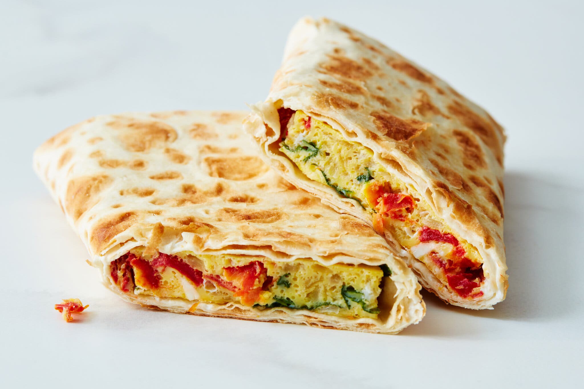 A folded flatbread wrap, cut in half, shows a filling of yellow eggs with red and green vegetables.