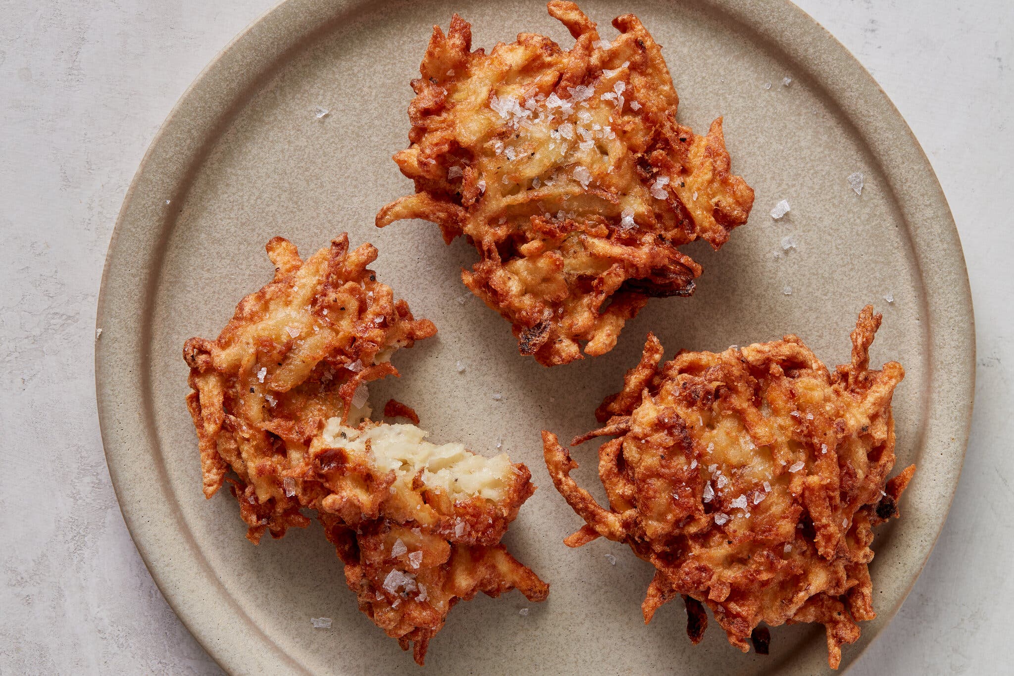 Three latkes on a neutral-colored plate, sprinkled with flaky salt.