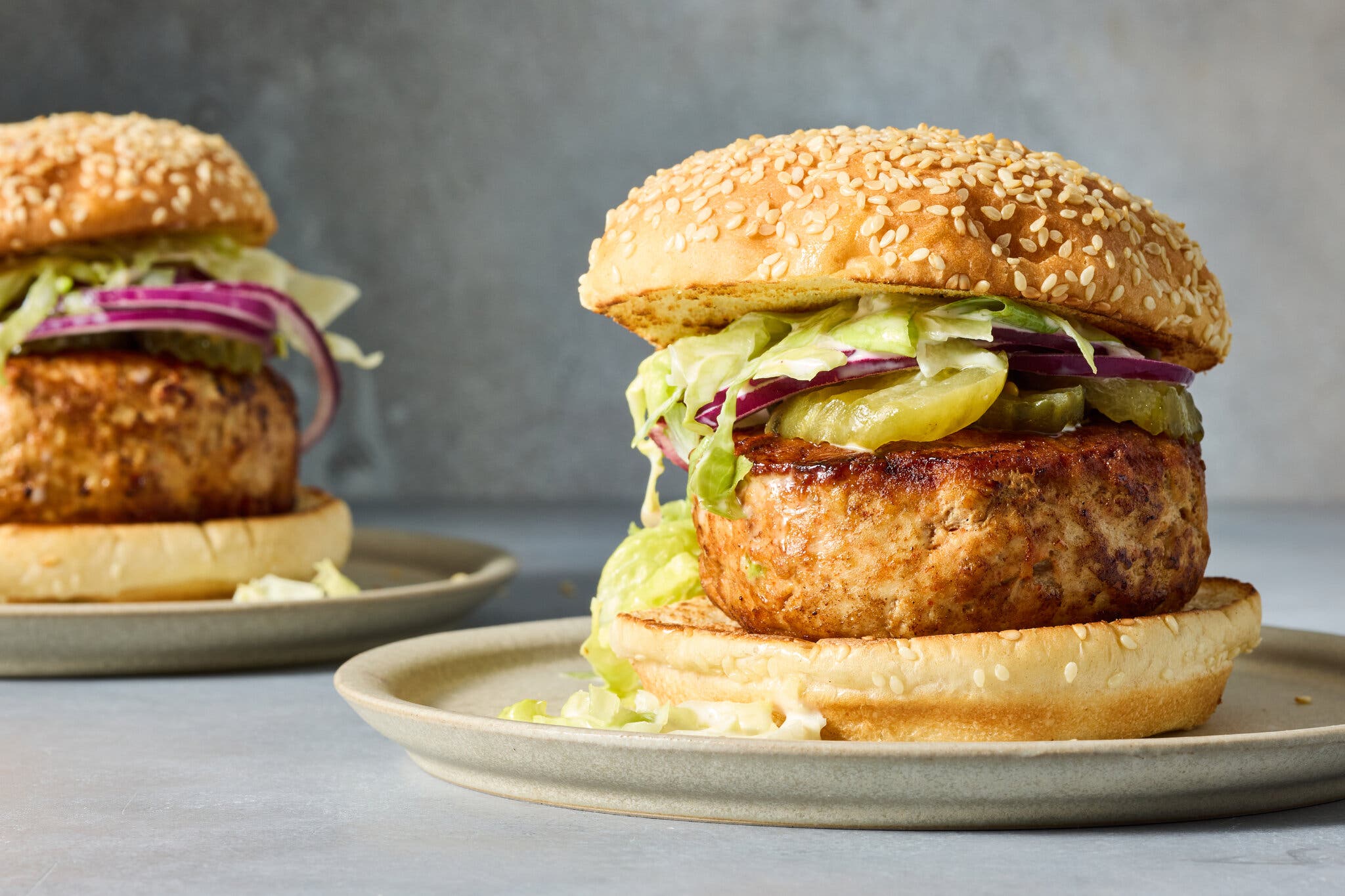 A thick turkey burger on a sesame bun with an iceberg lettuce slaw, on a plate. There is another burger on a plate in the background.