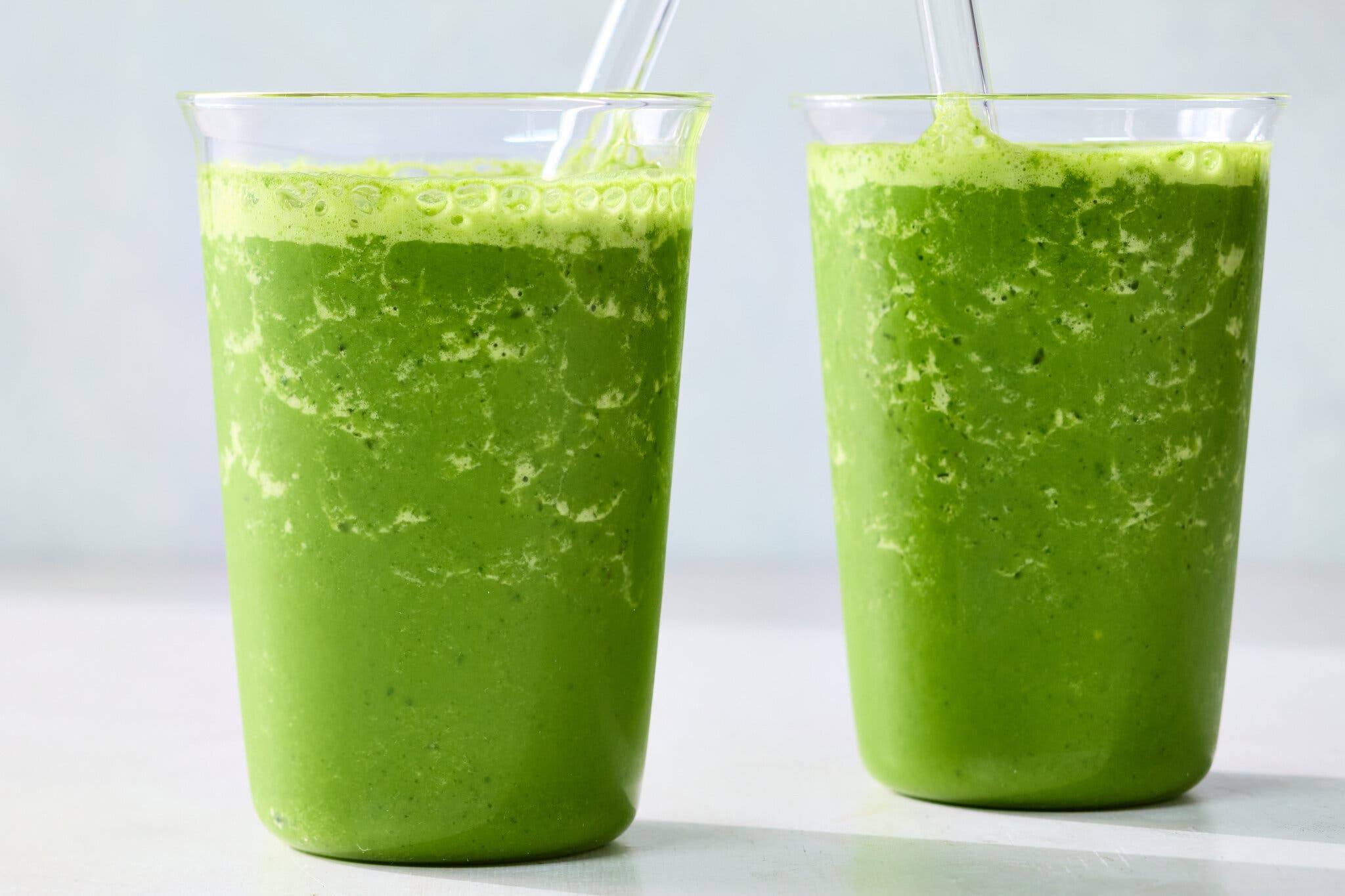 Two glass cups filled with green smoothies.