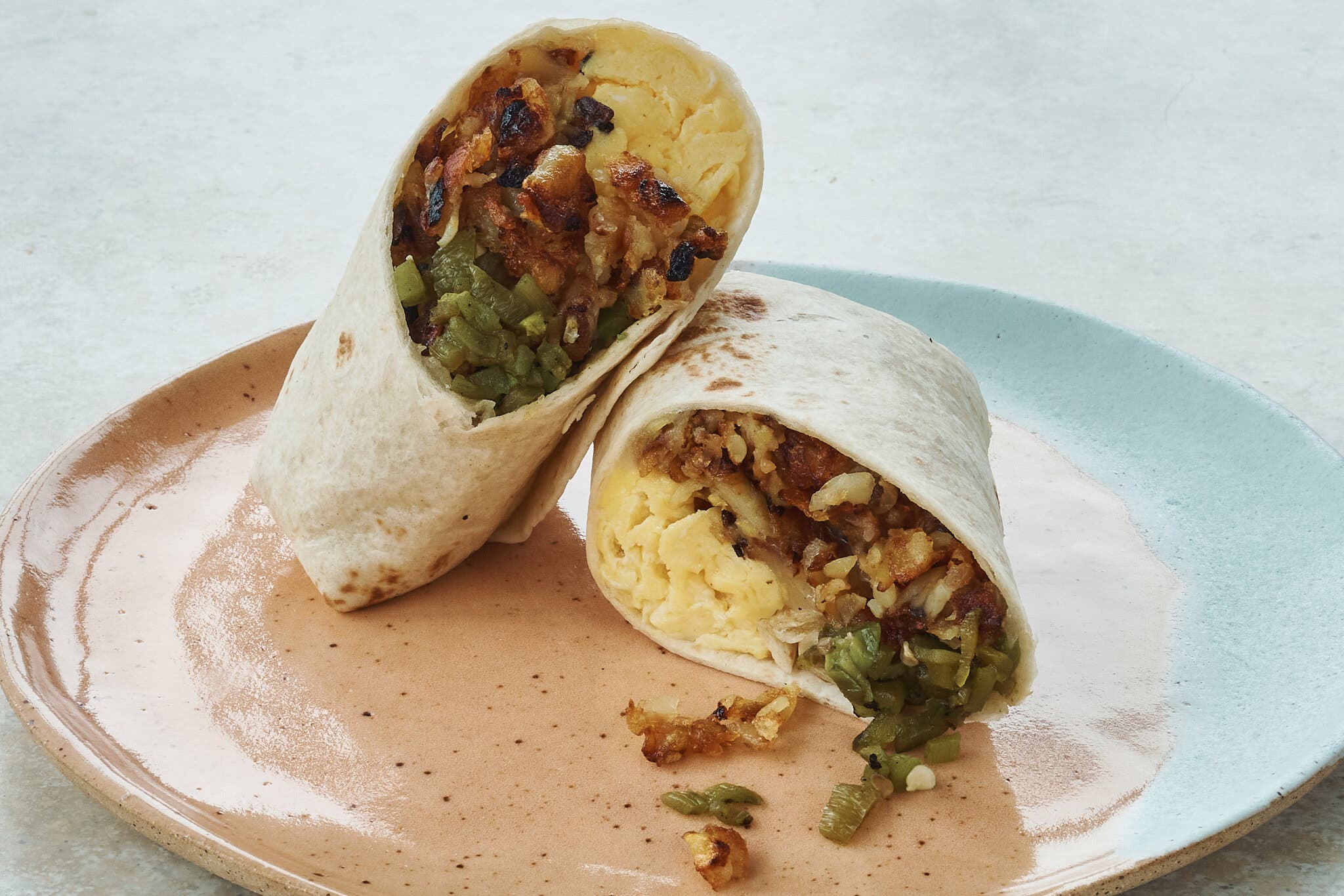 A New Mexico breakfast burrito has been cut in half and placed on a multicolor ceramic plate.